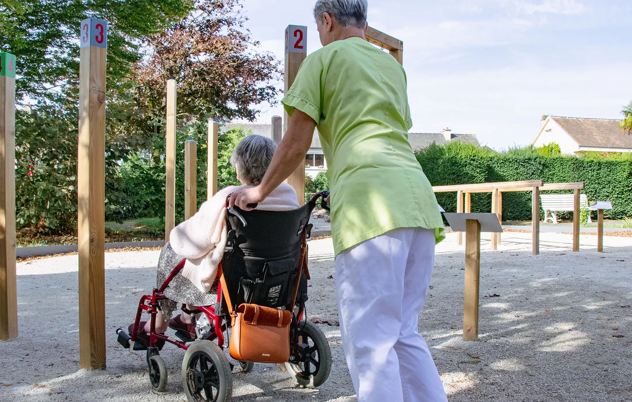 soignante poussant une résidente en fauteuil dans le parcours extérieur